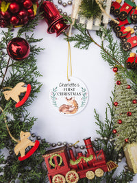 White circular ceramic ornament with the words (Name) First Christmas in the top center and the year. There is a mother dear snuggling her baby doe under the babies name.  Black cursive font.  Ships with gold threaded ornament tie.