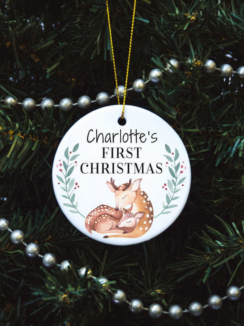 White circular ceramic ornament with the words (Name) First Christmas in the top center and the year. There is a mother dear snuggling her baby doe under the babies name.  Black cursive font.  Ships with gold threaded ornament tie.